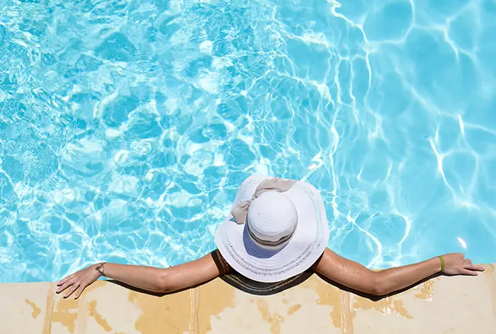 woman in a wide brim hat hanging out on the edge of a pool on a sunny day